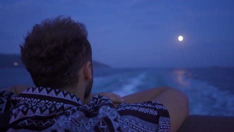 the man looking at the sea and the moon at night.