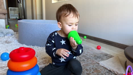 toddler boy plays with toy pyramid on the floor at home. kid pulls the toy to his mouth, then drops it and reaches camera.