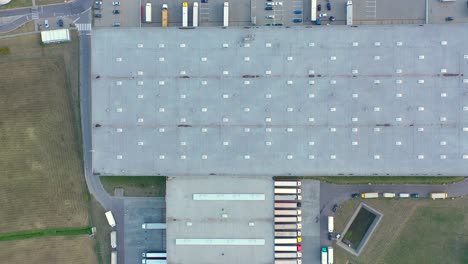 Semi-truck-with-cargo-trailer-is-travelling-on-a-parking-lot-along-a-warehouse-of-a-logistics-park