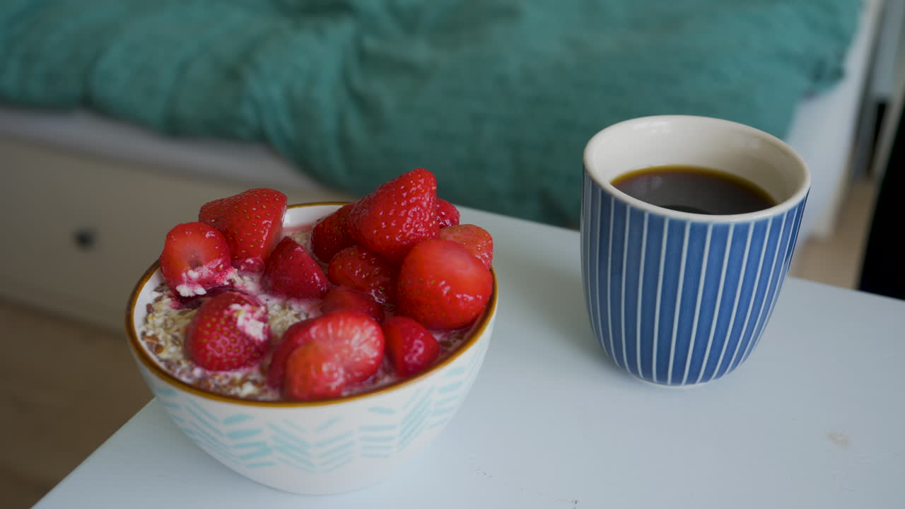 Coffee in a blue mug and dessert with strawberries in a white bowl and silver spoon.