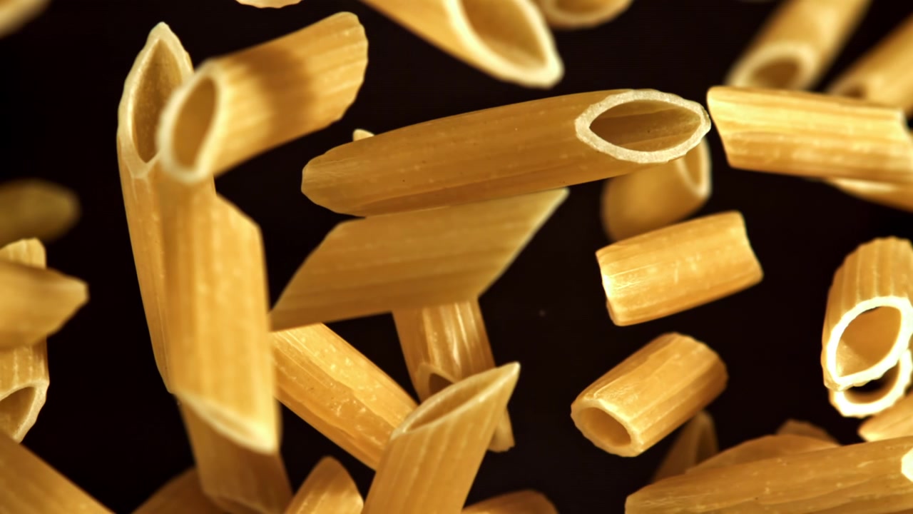 Penne crude che cadono al rallentatore su sfondo nero