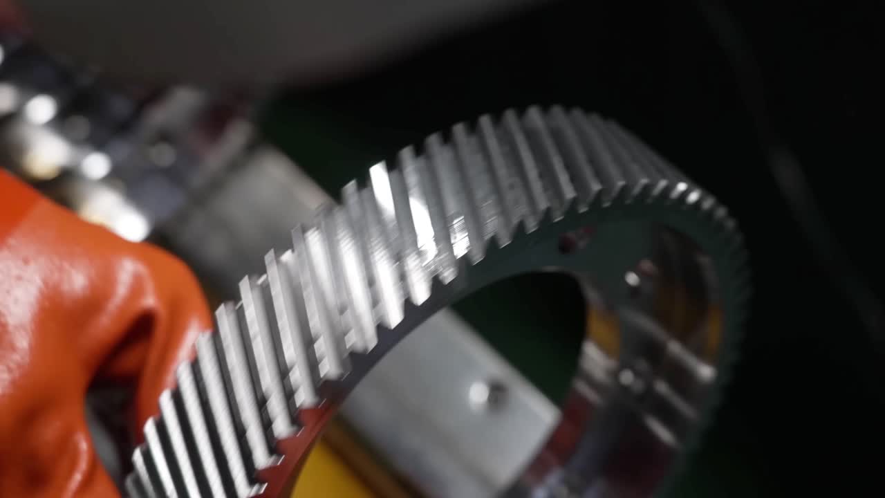 Close-up of a technician in orange protective gloves inspecting the teeth of a large precision-machined helical gear