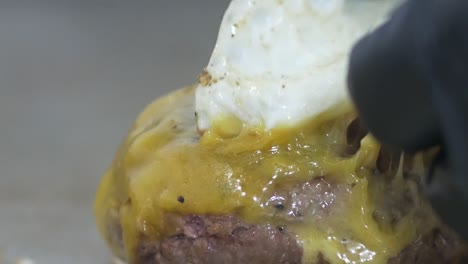 close-up of a chef's gloved hands as he adjusts the position of a fried egg atop a cooking gourmet burger