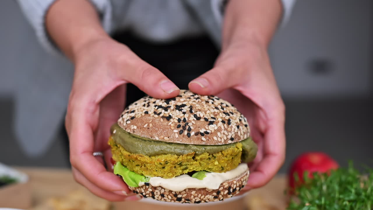 Delicious veggie burger is being put together with fresh greens and flavorful sauces. Nearby, healthy sides like salad and dried snacks complete the meal