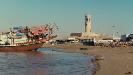 fishing dhow at coastal port with lighthouse and fort in oman