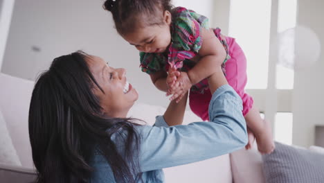 mother playing with baby daughter lifting her in the air at home