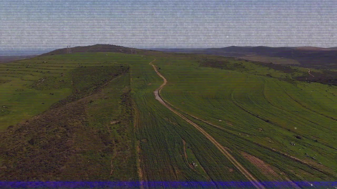 Po vzletu dron letí vpřed nad klikatou polní cestou, aby odhalil mozaiku polí.