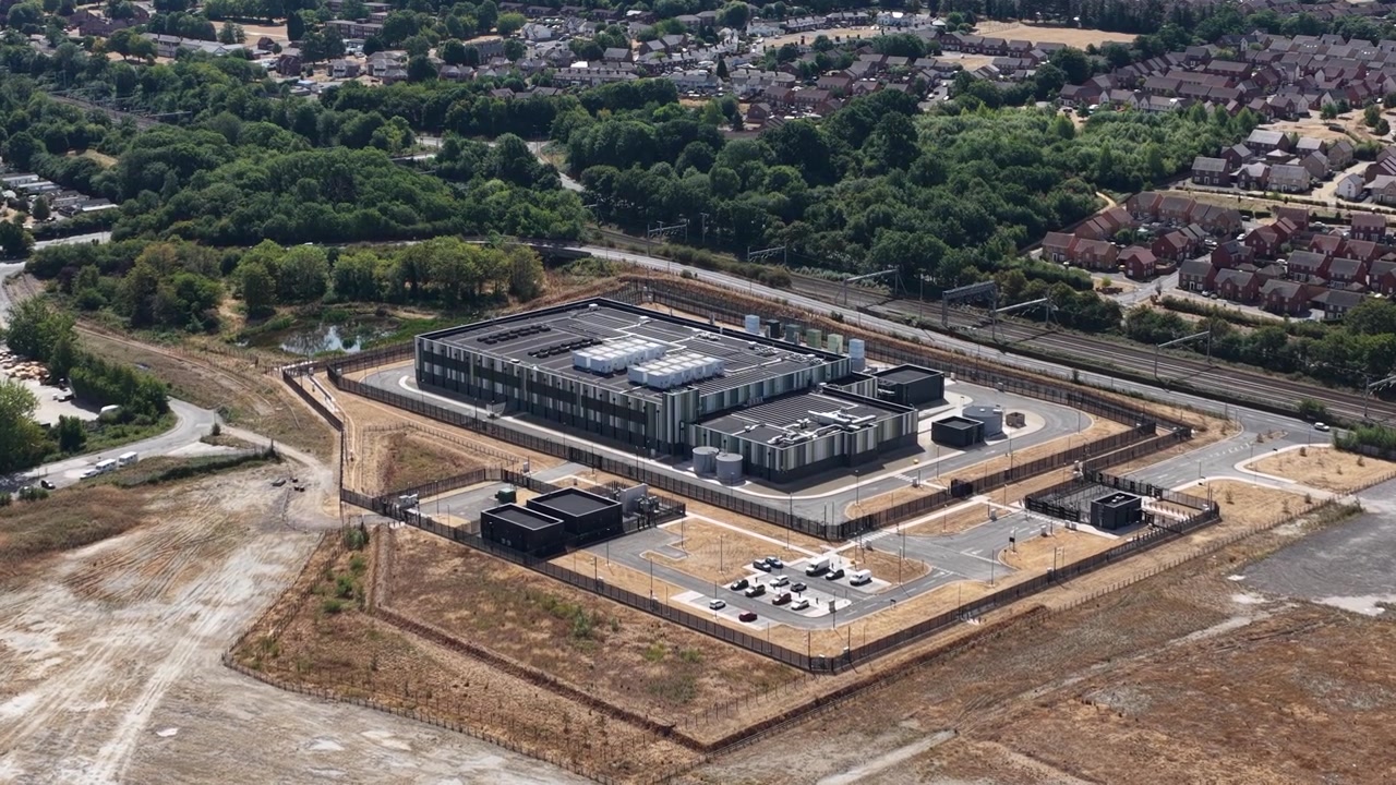 Dronebillede fra høj vinkel af et massivt datacenteranlæg med HVAC-køleenheder, transformerstationer og moderne arkitektur, der driver cloud-netværk og AI-systemer