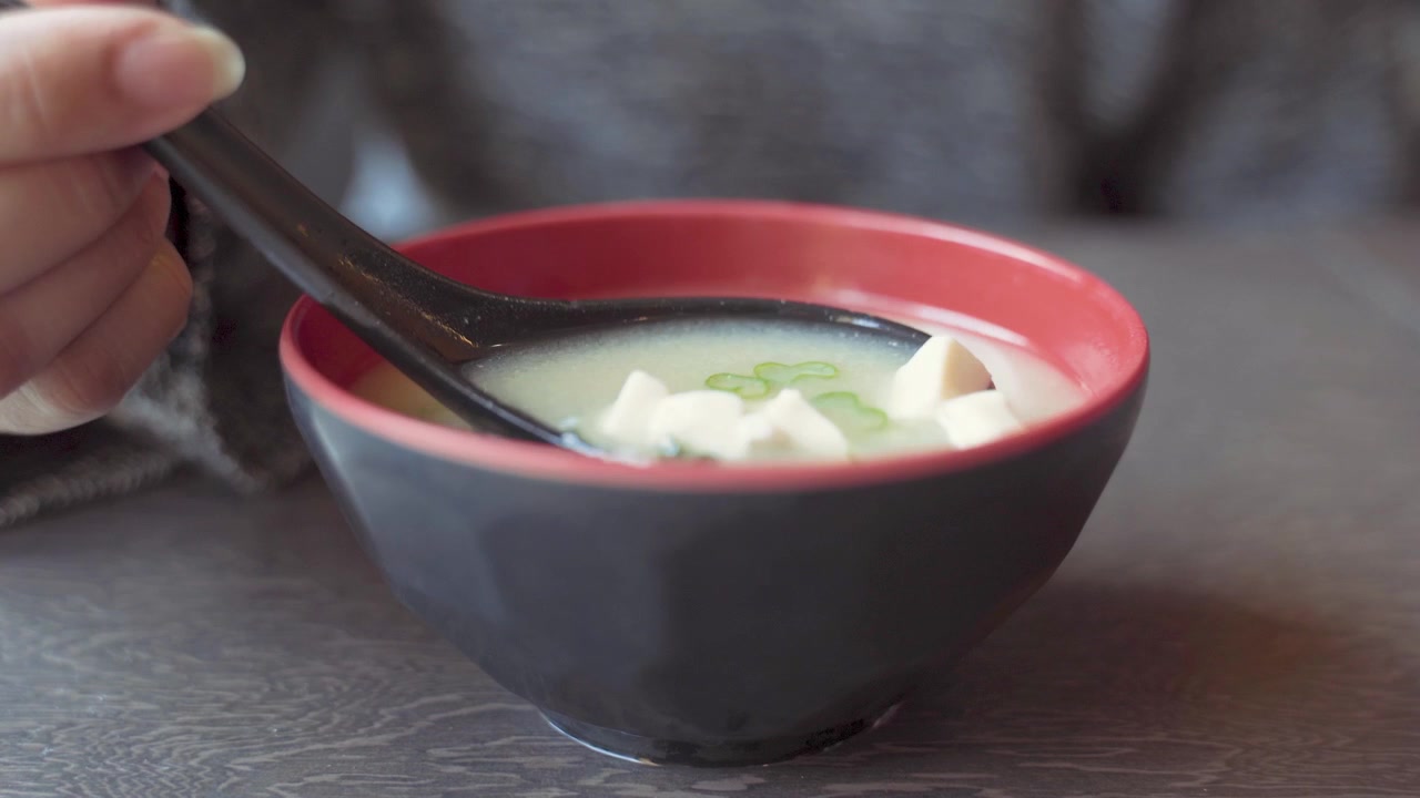 Tangan mungil wanita mengaduk sup miso dengan sendok di dalam mangkuk di restoran Jepang, bidikan jarak dekat