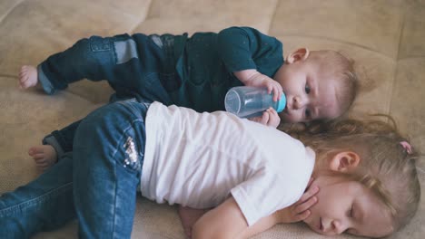 funny baby looks at sleeping sister drinking water on bed