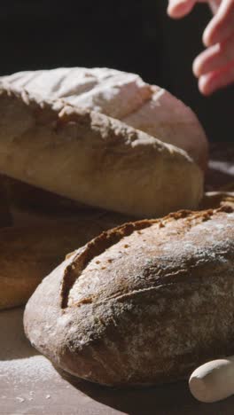 Low-Key-Aufnahme-Eines-Vertikalen-Videos-Einer-Person,-Die-Frisch-Gebackenes-Brot-Von-Der-Arbeitsfläche-Aufhebt