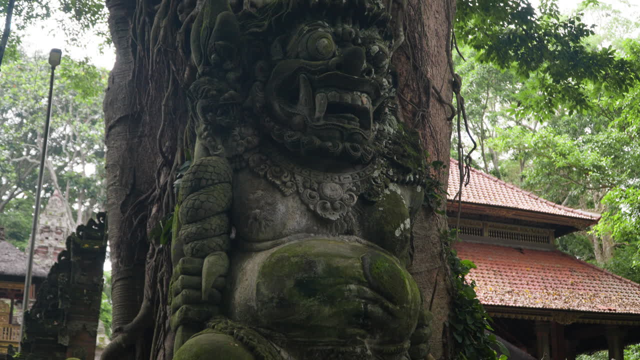 escultura cubierta de musgo junto al árbol en el santuario del bosque sagrado de monos en bali, indonesia