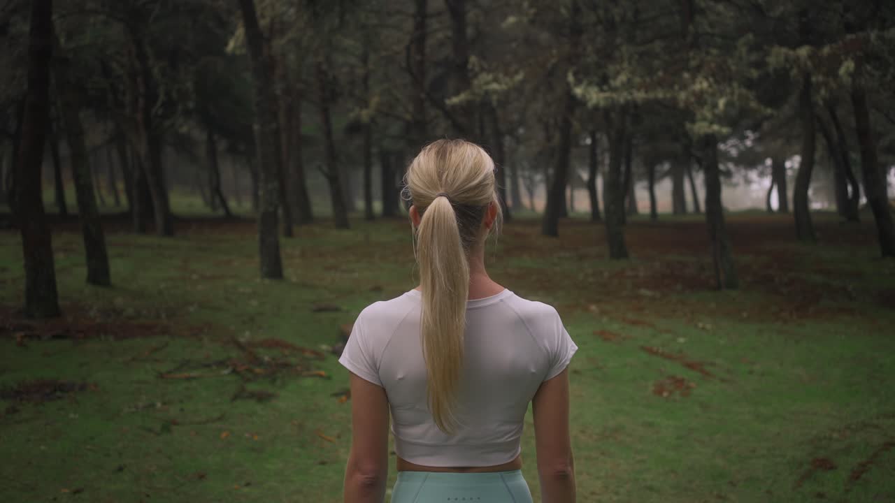 Behind lost fit woman standing in mysterious forest, looking at enchanted woods