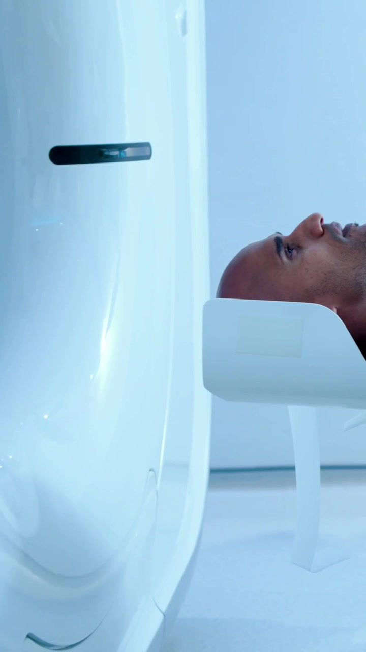 Vertical video: Advancing table moving patient into scanner in suite, gown on headrest, copy space