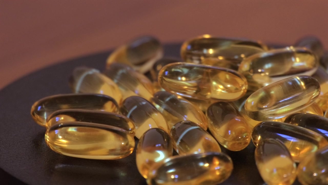 Fish oil capsules scattered on a dark tabletop, glowing under soft light