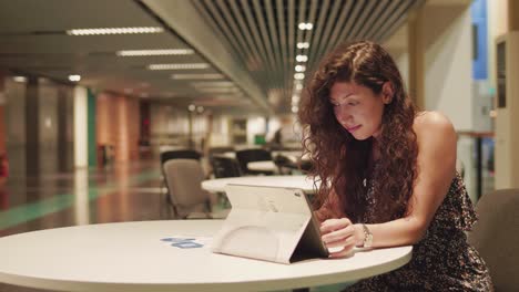 young pretty female sitting by a table and checking online messages on tablet