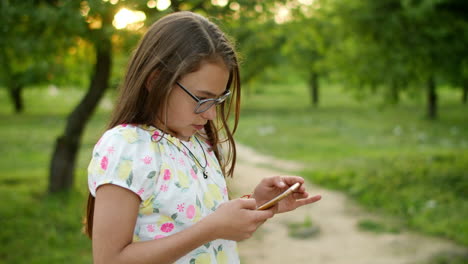 serious girl playing games on phone. concentrated girl standing in summer park