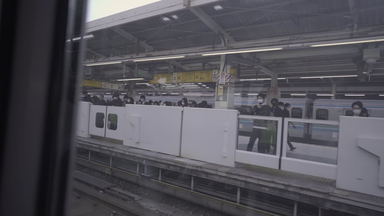 Japanese Train passing and commuter waiting at train station of Tokyo during early morning. Slow motion pan shot. Window shot out of train.