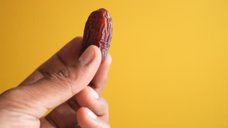 hand holding a single date against a yellow background