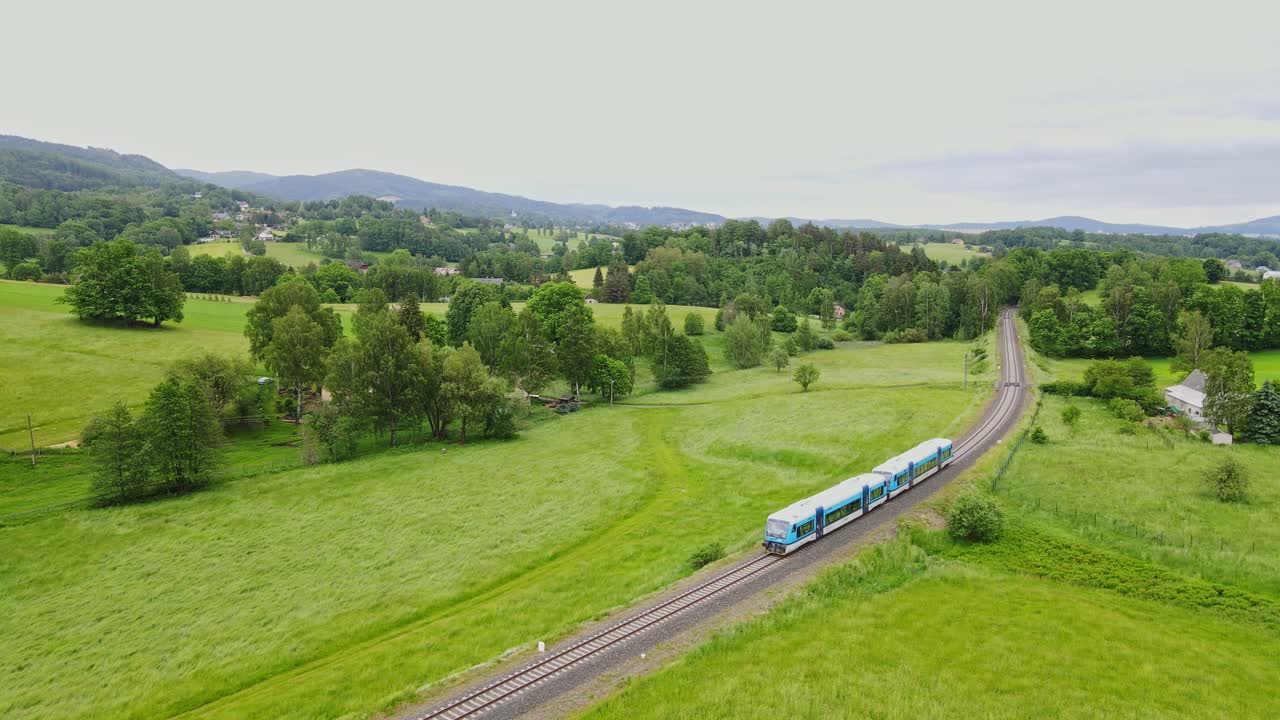 Aerial view of small blue train winding through lush fields in Czech countryside