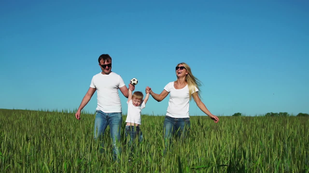 familia feliz: padre, madre e hijo, corriendo en el campo vestidos con camisetas blancas
