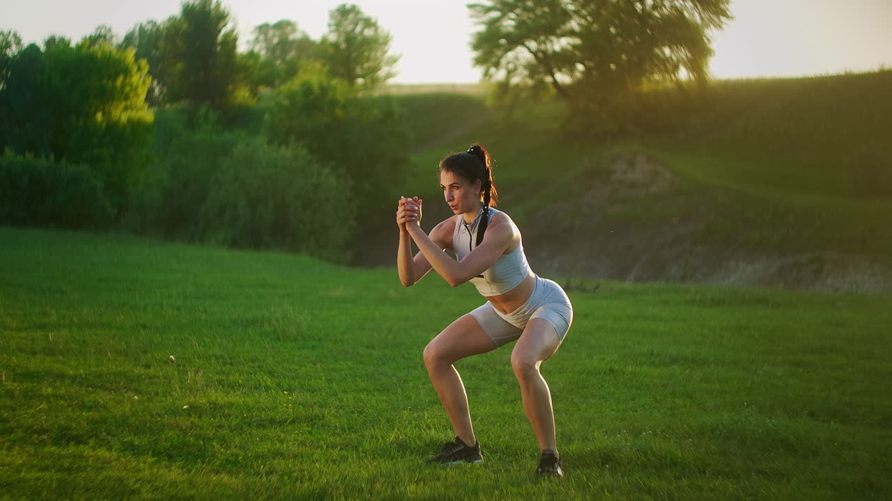 A young woman jumps a burpee exercise in a Park on the grass at sunset. Slow motion fitness training of a young woman in a meadow