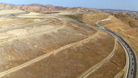 aerial view of a dry, hilly landscape with roads and a distant landfill area, with birds flying overhead