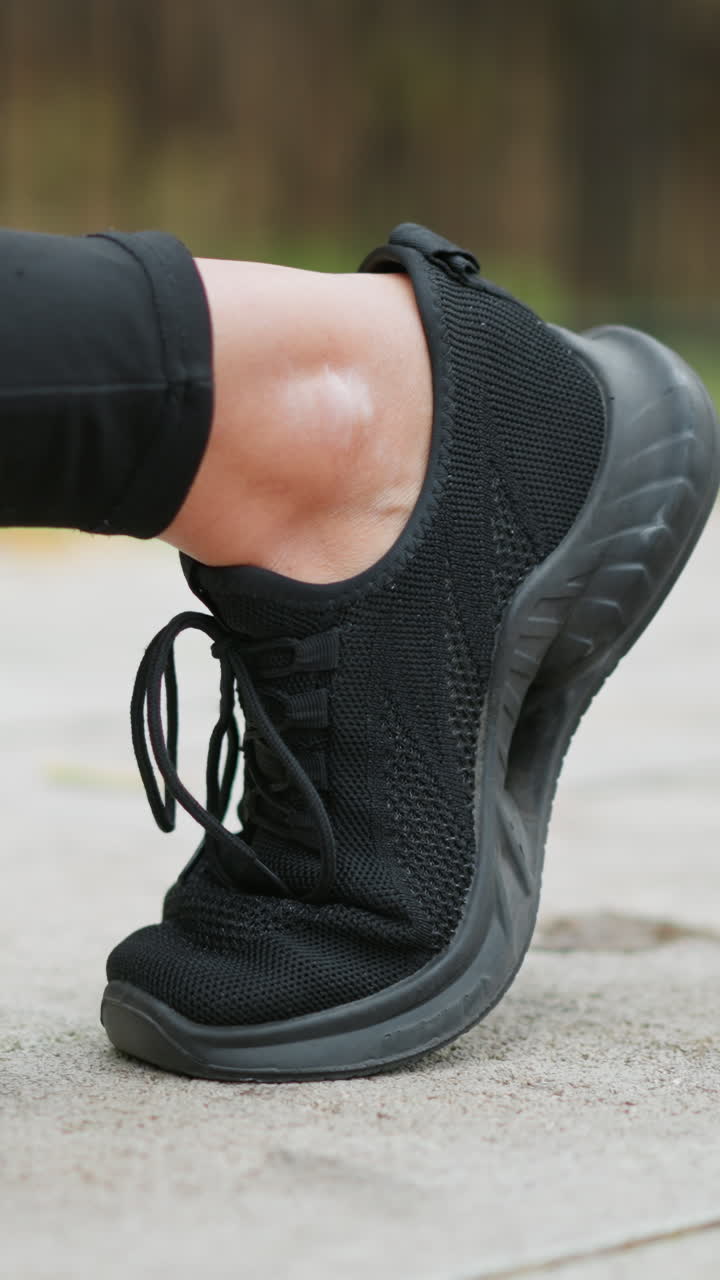 Primo piano del piede e delle scarpe da ginnastica di un corridore con la gamba piegata, mentre si prepara per una corsa su un percorso asfaltato liscio, mettendo in risalto le calzature sportive con uno sfondo naturale sfocato.