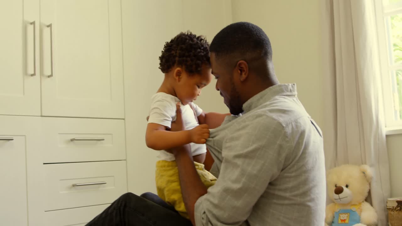 Vista laterale di un giovane padre di colore che gioca con il figlio sul pavimento in una casa confortevole 4k