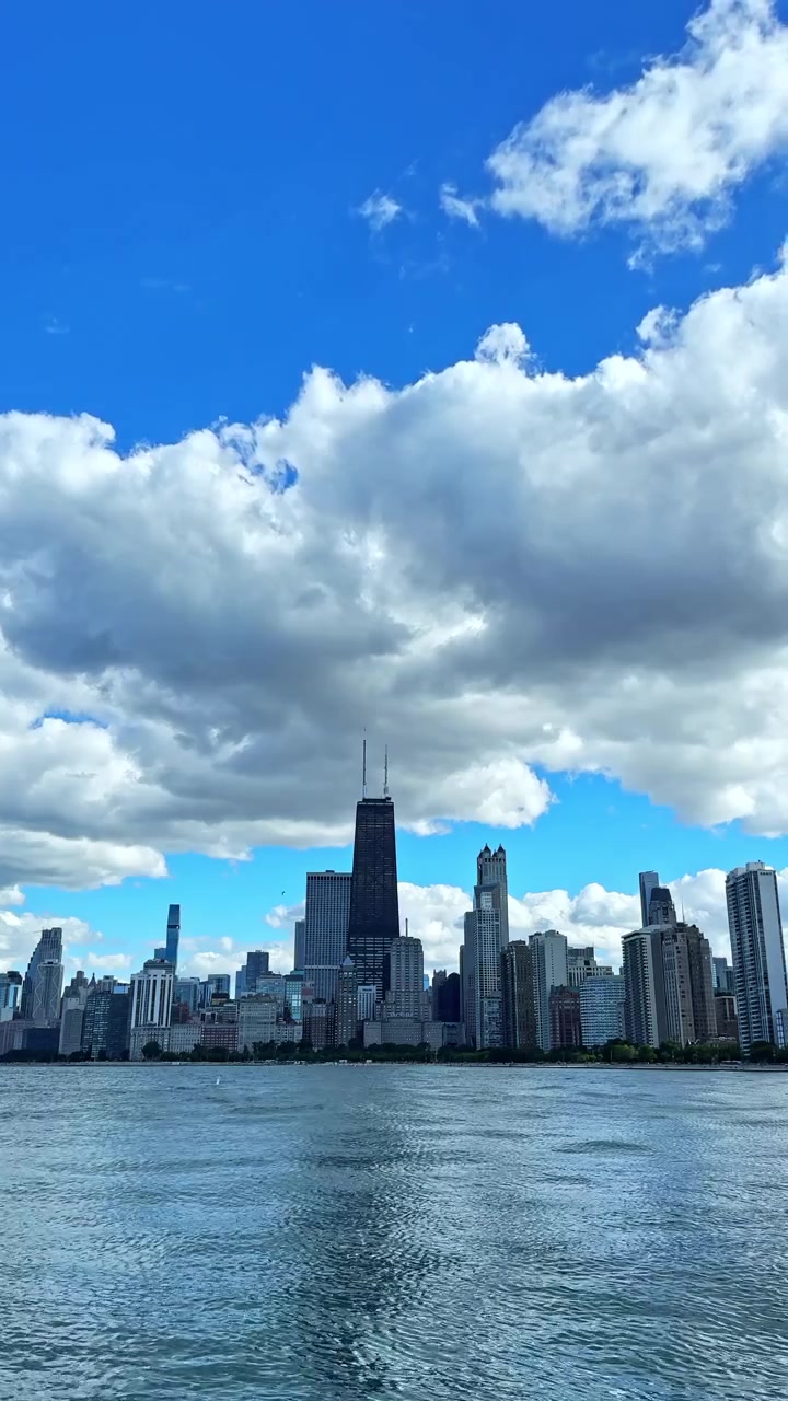 Vista do horizonte de Chicago com nuvens no céu e água em primeiro plano, tirada à distância durante o dia.