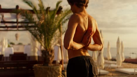 Guy-guy-doing-stretching-and-meditating-on-a-sunny-beach-in-the-morning.-The-yogi-holds-his-hands-behind-his-back-in-a-special-yoga-pose