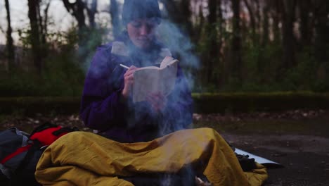 joven mochila haciendo notas en el fuego del campamento