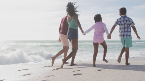 Back-view-of-hispanic-mother,-father,-son-and-daughter-holding-hands-and-walking-on-beach