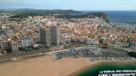 calonge's cityscape unfolds beneath a clear sky, revealing a mix of traditional and modern architecture, a sandy beach, and boats moored in the harbor