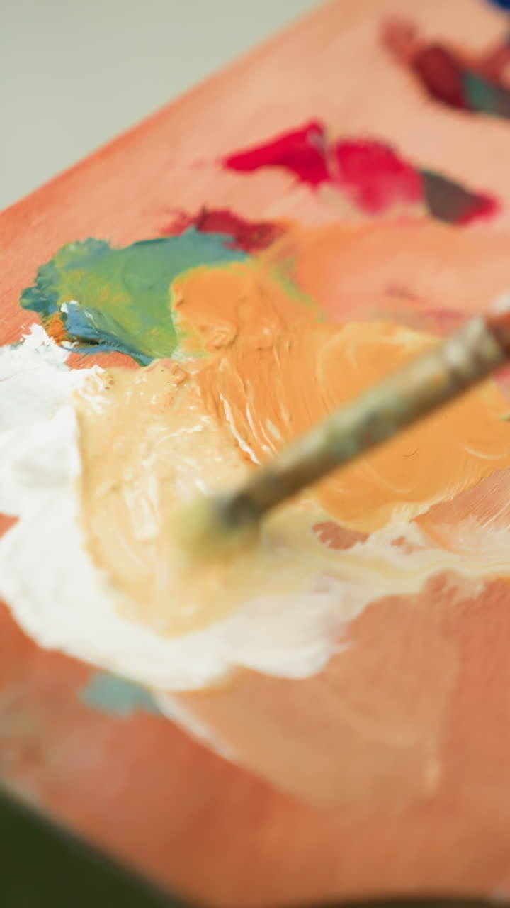 A close-up shot of an artist s hand holding a wooden palette while mixing various shades of paint with a small brush. The focus on the palette and brush