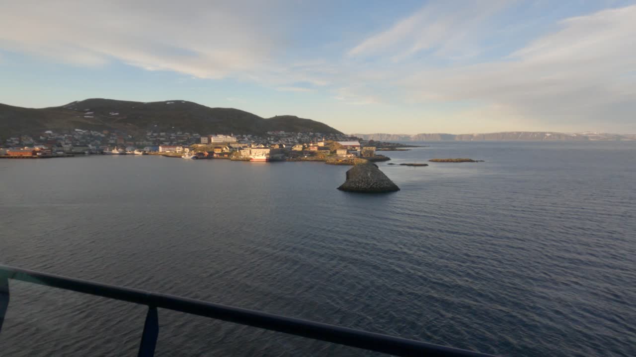 Veduta aerea di Honningsvåg, la città più settentrionale della Norvegia, adagiata contro dolci colline con le calme acque dell'Oceano Artico e un cielo drammatico all'ora d'oro.