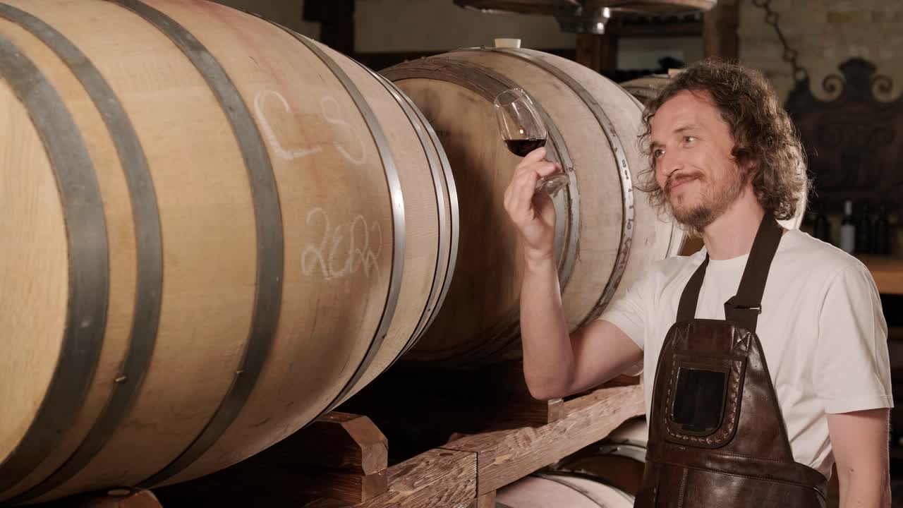 성공한 남성 소멜리어의 진정한 은 맛을 맛보고 와인 지하실에서 투명한 유리통에 부어 놓은 화이트 와인의 품질을 확인하는 것입니다.