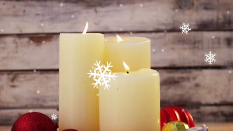 Animation-of-three-lit-candles,-snowflakes-falling-over-wooden-surface