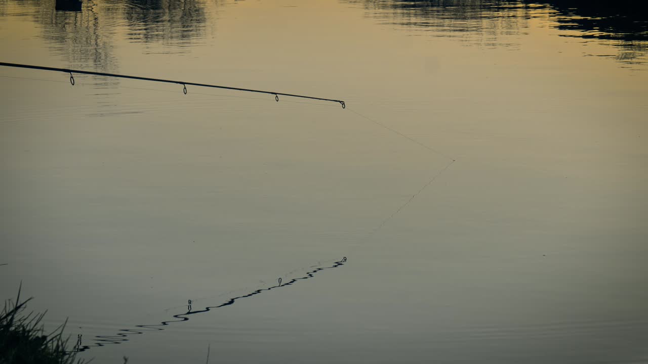 Angelrute über ruhiger Wasseroberfläche, die sanftes goldenes Licht reflektiert.