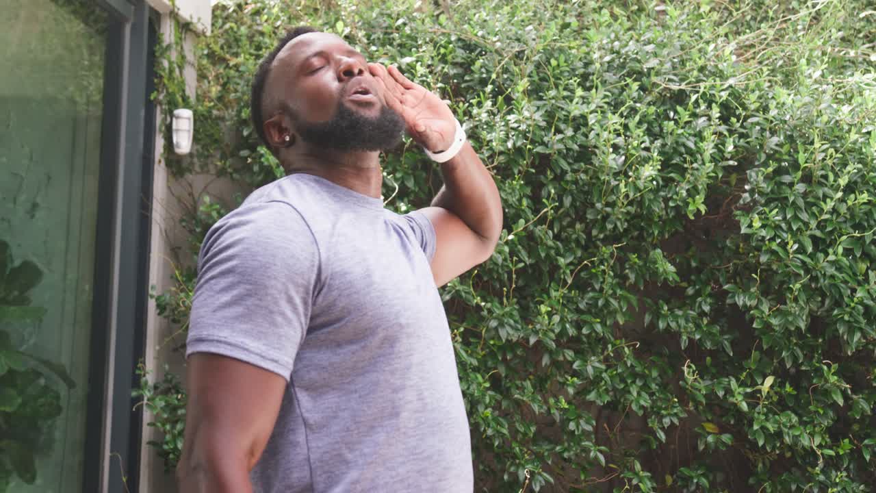 African adult male feeling overheated on sunny patio, holding green water bottle, pressing forehead