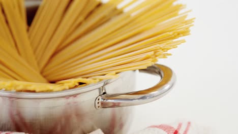 raw spaghetti arranged in silver pot places on red and white napkin on white background