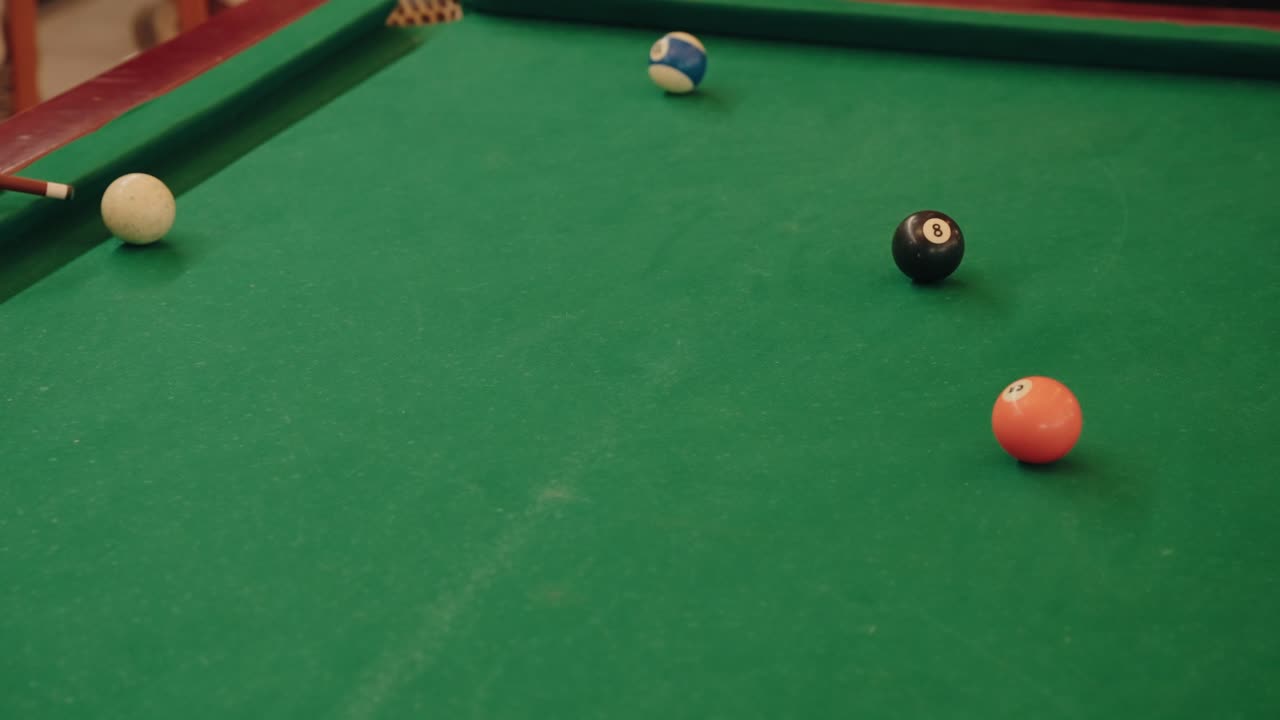 Billiard cue aiming at white ball with 8 ball and other balls scattered on green pool table