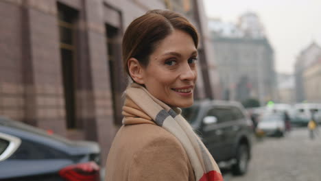 rear view caucasianbusinesswoman wearing coat and scarf walking on the street, then she turns to the camera and smiles