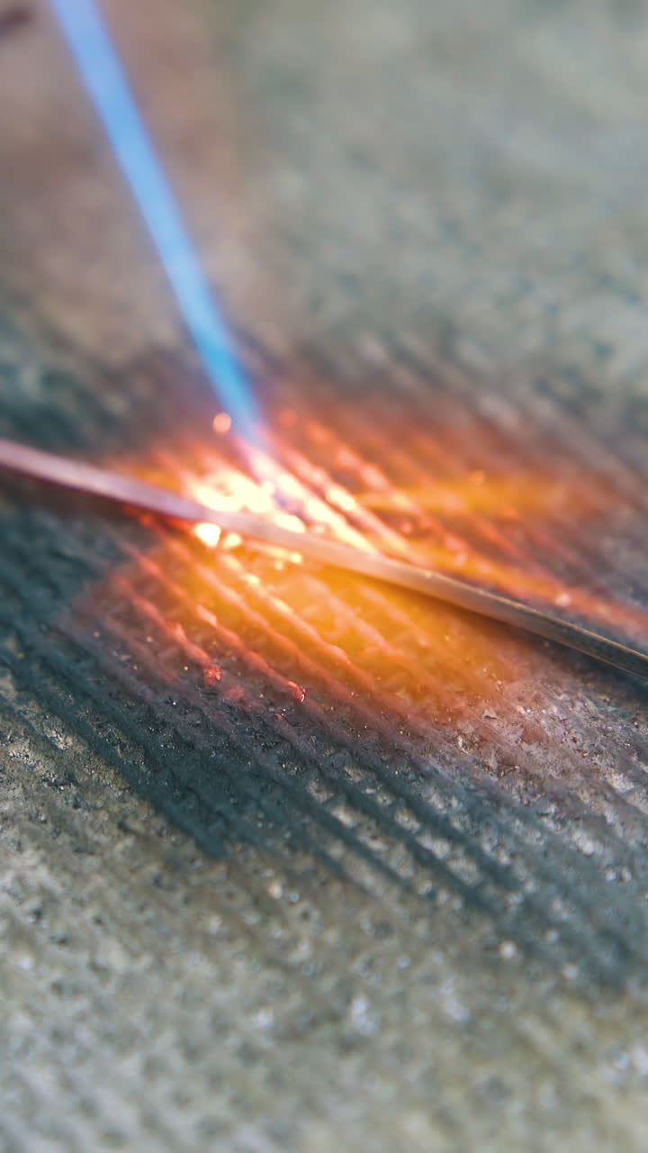 CU shot: heating of gold metal rod with gas burner flame on fireproof asbestos material on table in jewelry workshop closeup