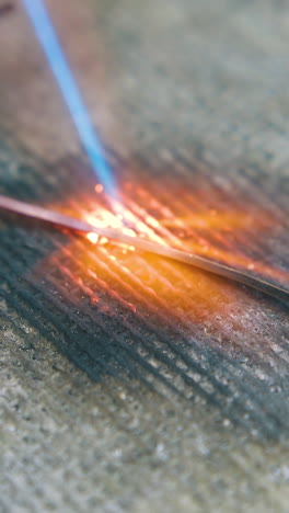 cu shot: heating of gold metal rod with gas burner flame on fireproof asbestos material on table in jewelry workshop closeup