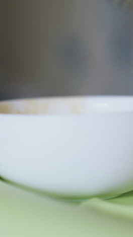 woman takes tasty fresh cream soup with spoon from white bowl to feed baby at green plastic table extreme close view