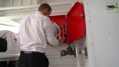 Ships-captain-inspecting-firehose---Firefighting-equipment-onboard-passenger-ship-is-controlled---Static-low-angle-looking-up-at-box-and-male-captain