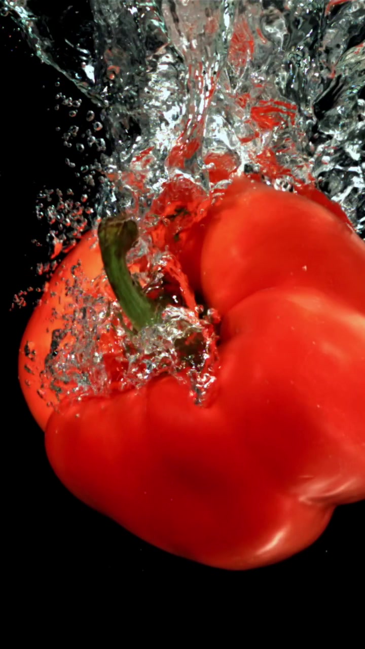 Červená paprika padající do vody s cákanci a bublinkami