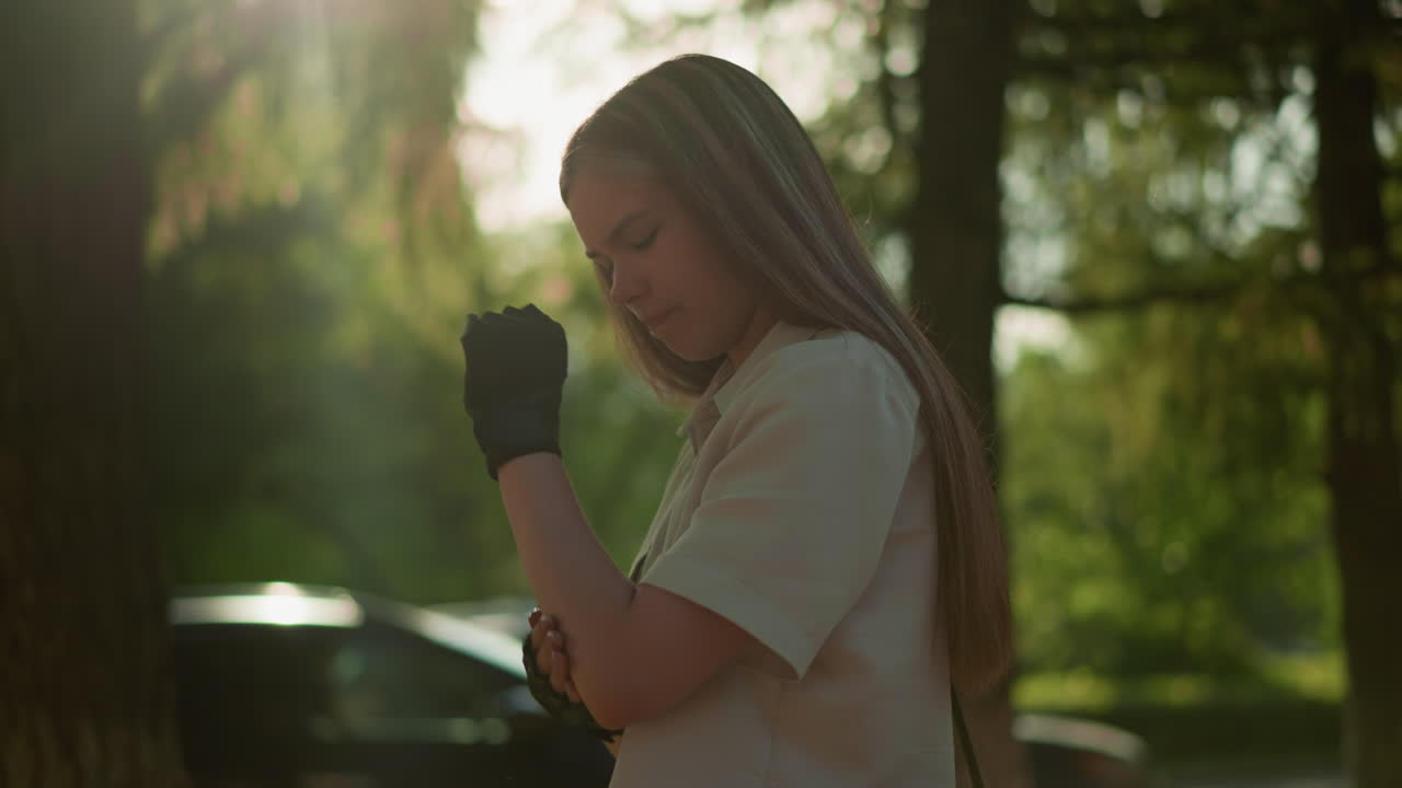 검은 장갑을 입은 젊은 성인은 잎을 통해 필터링되는 빛으로 팔꿈치를 문지르고, 그녀에게 따뜻한 빛을 아, 움직이는 차와 함께 흐릿한 배경