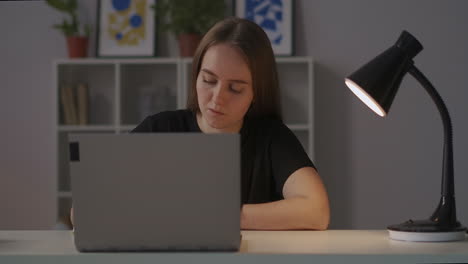 Una-Mujer-Está-Estudiando-Escribir-Notas-En-Línea-En-Casa-Por-La-Noche-Sentada-En-La-Mesa-Toma-Panorámica-Alrededor-De-Su-Retrato-Medio-De-Un-Estudiante-De-Aprendizaje